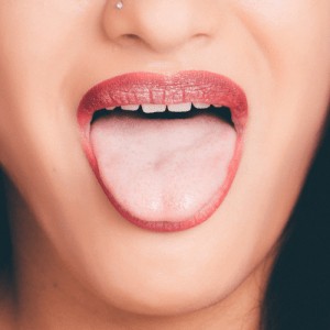 Woman wearing brownish-pink lipstick sticking her tongue out. Shot of nose, mouth and teeth.