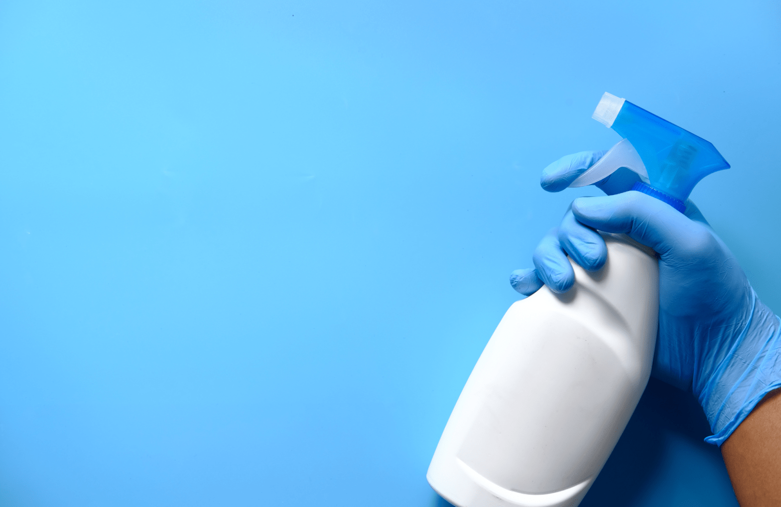 White spray bottle, blue glove holding it.