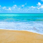 Sandy beach with blue water and bright blue sky.