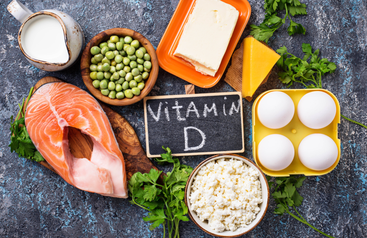 Vitamin D written on a chalk board, surrounded by food sources like salmon, eggs and cheese.