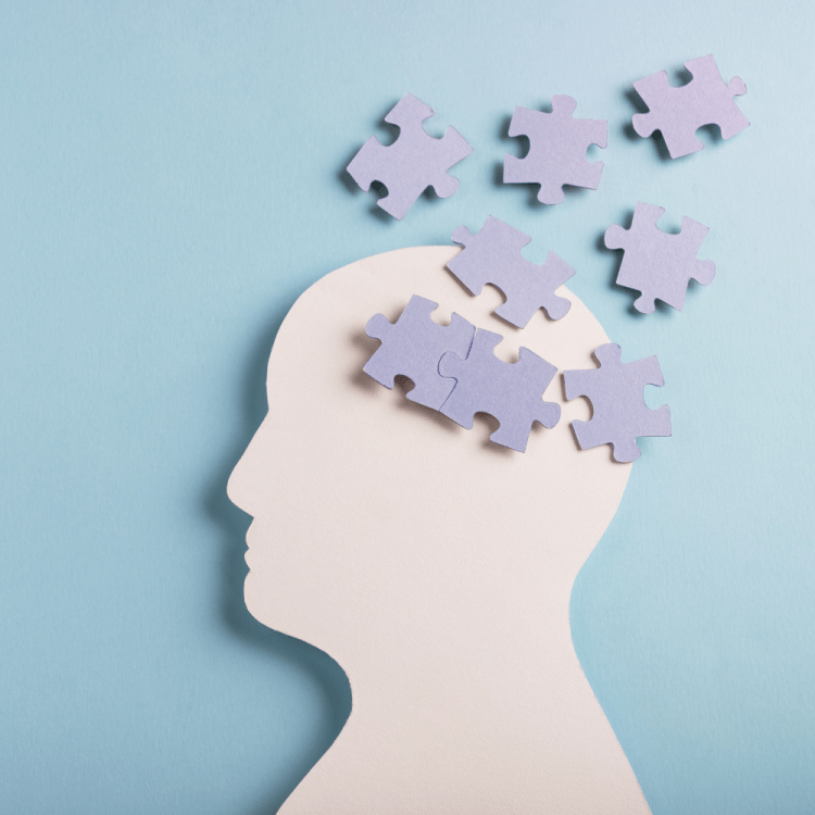 Puzzle pieces scattered over where the brain should be on a paper cut out of a head.